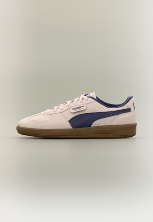 Zapatilla beige Puma Palermo con franja lateral azul oscuro y suela marrón, mostrada desde el lado interior sobre fondo liso.