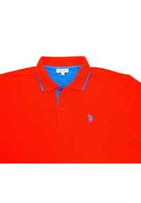 Červené polo tričko s modrým límcem, dvouknoflíkovou légou a malým modrým vyšitým logem na levé hrudi. Hladká bavlněná tkanina.