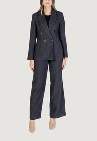 Blazer grigio scuro a doppio petto con vestibilità su misura e rever, abbinato a pantaloni a gamba larga. Texture liscia e dettagli con bottoni argentati.