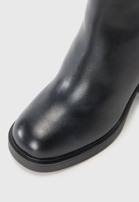 Zwarte leren enkelboot met een glanzende afwerking, ronde neus en een textuurrubber zool. Kenmerkt zich door minimale stiksels en een slank profiel.
