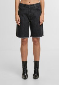 Shorts de mezclilla negra con dobladillo deshilachado, cintura a media altura, dos bolsillos delanteros y cierre de botón. Combinados con botas negras brillantes hasta el tobillo.