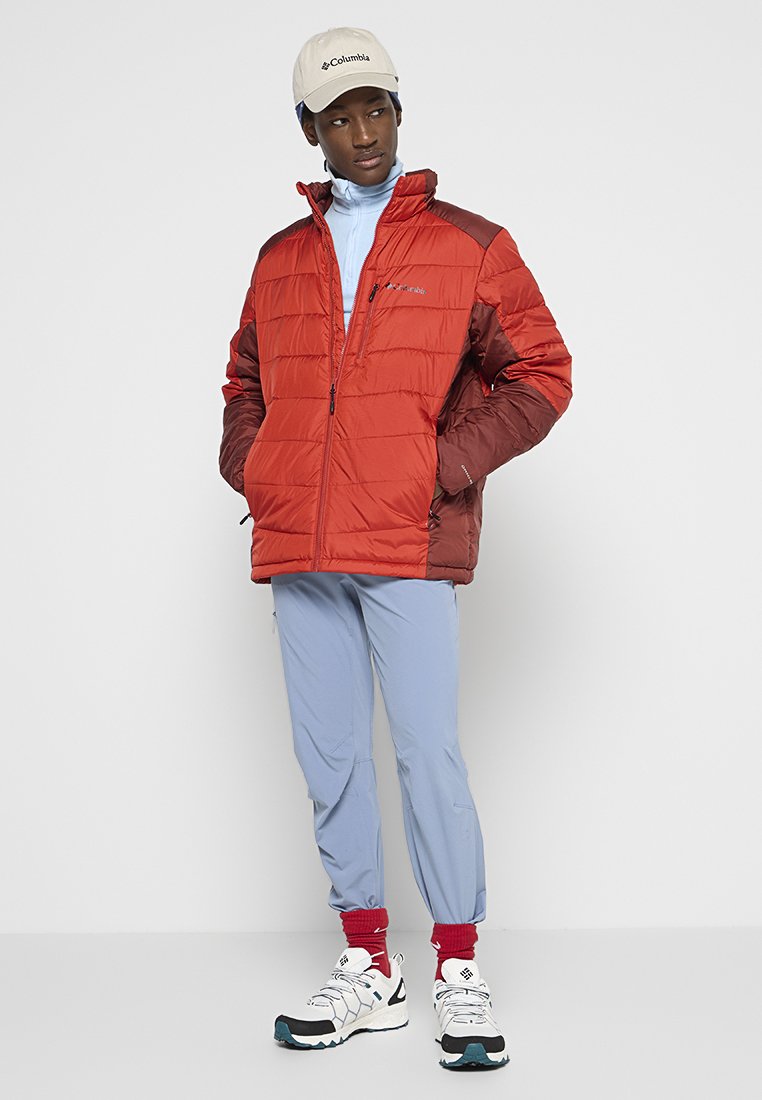 Czerwono-brązowa kurtka ocieplana na zamek, jasnoniebieska warstwa podstawowa, jasnoniebieskie spodnie oraz białe sneakersy z czarnymi akcentami.