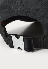 Black cap with a textured fabric, featuring a silver metal buckle clasp and adjustable strap for fit. Inside is a contrasting red lining.