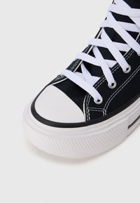Sneaker in tela nera con punta in gomma bianca, lacci bianchi e cuciture a contrasto. Presenta una suola bianca con texture e una striscia nera di accento.