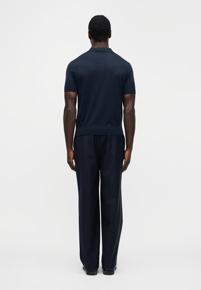 Μπλε ναυτικό πόλο με κοντά μανίκια συνδυασμένο με παντελόνι με λεπτές ρίγες, και τα δύο με εφαρμοστή γραμμή και λεία υφή.