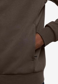 Brown sweatshirt with a textured fabric, featuring a side pocket and ribbed cuffs. The design is casual and fitted around the torso.