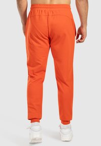 Orange joggingbyxor i en blandning av bomull, med elastisk midjeband, avsmalnande passform och ribbade muddar. Kombinationen bärs med vita sneakers.