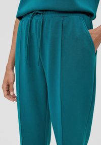 Teal joggings met een elastische tailleband, trekkoord en zijzakken; gladde textuur en losse pasvorm; subtiele plooien aan de voorkant.