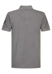 Graues Poloshirt mit kurzem Kragen, kurzen Ärmeln und einem Patch auf dem linken Ärmel. Der Stoff hat eine glatte Textur mit Steppnähten.