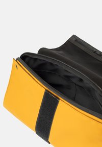 Borsa gialla realizzata in materiale resistente, con una cerniera nera e un interno nero. L'esterno presenta un accento in velcro nero.