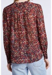 Blouse à manches longues et transparente avec un fond noir et un motif floral coloré. Tissu doux avec une coupe décontractée et des détails froncés.
