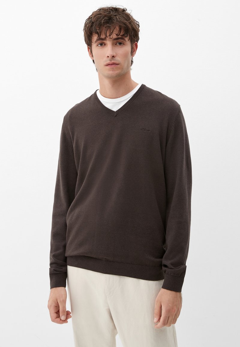 Brauner V-Ausschnitt-Pullover aus weichem Material, mit langen Ärmeln und gerippten Bündchen, getragen über einem weißen T-Shirt. Glatte Textur mit minimalen Details.