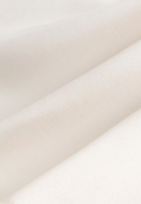 Jasnobeżowa tkanina o gładkiej fakturze, ukazująca złożone warstwy z delikatnym wzorem tkania.