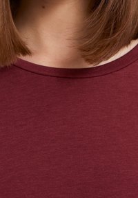 Bordeaux ribbel trui met korte mouwen en een ronde halslijn. Zachte textuur en aansluitend ontwerp. Geen zichtbare patronen of accenten.