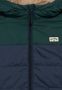 Jaka s postavom u tamnozelenoj i tamnoplavoj boji, s patentnim zatvaračem i malom robnom oznakom na prsima. Glatka tekstura s kapuljačom.