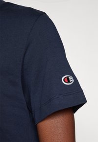 Navyblauw katoenen t-shirt met een ronde hals en korte mouwen, voorzien van een klein geborduurd logo in rood, wit en zwart op de linker mouw.