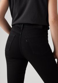 Jeans de mezclilla negra con un diseño ajustado, detalles de costura sutiles, dos bolsillos traseros y una cintura alta. Pantalones mostrados desde la parte posterior.