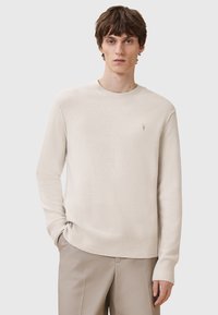 Hellbeige Strickpullover mit Rundhalsausschnitt, gerippten Bündchen und Saum, featuring ein kleines Logo auf der linken Brust. Glatte Textur, lässiges Design.