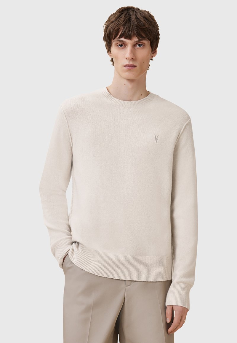 Hellbeige Strickpullover mit Rundhalsausschnitt, gerippten Bündchen und Saum, featuring ein kleines Logo auf der linken Brust. Glatte Textur, lässiges Design.