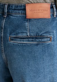 Denim jeans in medium blauw met een zichtbaar leren label met de tekst "Marc O'Polo," met een enkele achterzak met contrasterende stiksels.