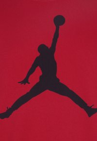 Camiseta de tela roja con una gran silueta negra de una persona saltando con un balón de baloncesto, mostrando movimiento y diseño atlético.