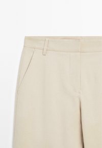 Beige broeken gemaakt van een gladde stof, met een recht model, zijzakken en subtiele gestikte accenten langs de tailleband.
