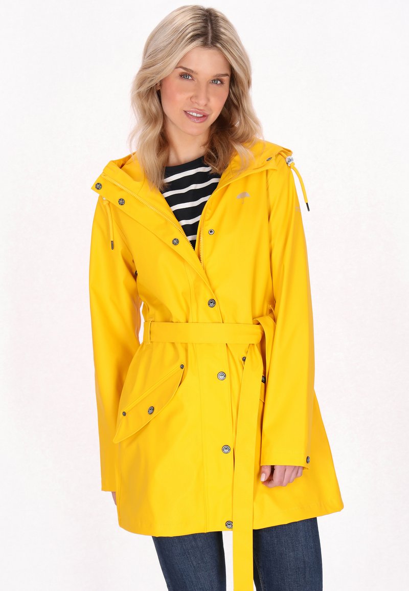 Rumena vodoodporna dežni jakna s kapuco, pasom z zaponko, snap gumbi in velikimi stranskimi žepi. Obuta je čez črno-belo črtasto majico.