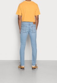 Ljusblå denimjeans med slim fit, bärs tillsammans med en gul t-shirt. Har två bakfickor och en brun läderlogg.