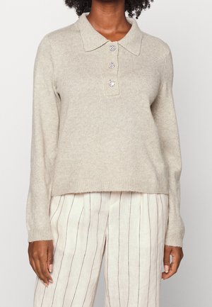 Suéter de punto beige de manga larga con cuello y tres botones decorativos, combinado con pantalones blancos que tienen rayas verticales delgadas.