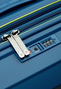 Valigia rigida blu con superficie texturizzata, doppi cursori della cerniera in argento, accenti gialli e lucchetto a combinazione con simbolo TSA.