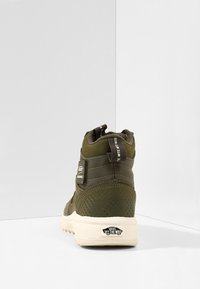 Zapatillas altas verdes con material texturizado, talón reforzado, parche con logo y suela color crema. Presenta una lengüeta para facilitar el calzado.