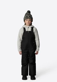 Black insulated snow overalls with adjustable straps, paired with a white fleece hoodie. A black and white patterned knit beanie completes the look.