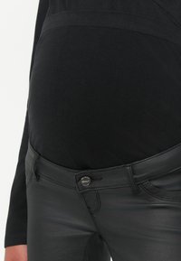 Zwarte, strakke broek met een glanzende textuur. Heeft een vlakke tailleband en een metalen knoop met "ONLY"-branding aan de voorkant.