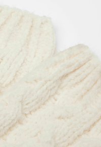 Tissu côtelé de couleur crème tricoté, texture douce, présentant un motif épais et une apparence duveteuse, adapté à un port hivernal.