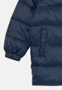 Giacca imbottita blu navale con polsini elasticizzati, una tasca laterale, texture liscia e motivo a righe orizzontali.