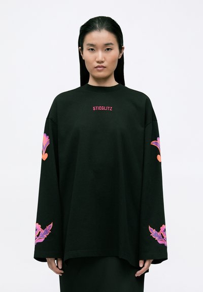 Sweatshirt oversized negru cu mâneci lungi, având broderie florală colorată pe mansete și textul "STIEGLITZ" în roz pe piept.
