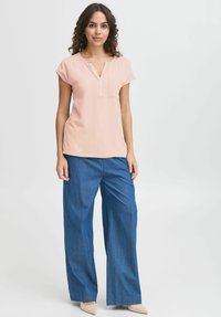 Blusa rosa chiaro con scollo a V e maniche corte, abbinata a pantaloni in denim blu a gamba larga. Tessuto morbido con dettaglio della tasca.