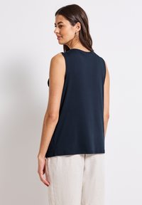 Top senza maniche di colore blu navy in un tessuto liscio con una vestibilità comoda, caratterizzato da un collo rotondo e dettagli di cucitura sottili. Abbinato a pantaloni leggeri in lino.