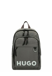 Zaino in nylon grigio con zip nere e una tasca frontale. Grande logo bianco "HUGO" e tracolla a contrasto con branding.