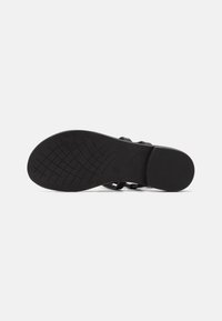 Black sandal with a textured rubber sole, featuring wide straps and a flat design. Notable for its minimalist look and sturdy construction.