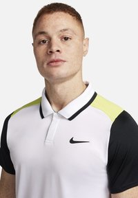 Polo bianco con maniche nere e un accento giallo neon. Presenta un logo Nike nero sul petto e un design di colletto classico.