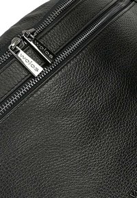 Angolo di una borsa in pelle nera testurizzata con due zip argentate dotate di tiranti marchiati, che evidenziano una finitura liscia e resistente.