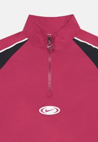 Pulover s četrt zadrgo v svetlo roza barvi z visokim ovratnikom, belimi in črnimi detajli ter logotipom Nike na sprednji strani. Gladka tekstura.