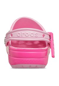 Crocs rosa con superficie testurizzata, fascetta regolabile sul tallone e logo prominente. Presentano una suola rialzata con motivo circolare per una migliore aderenza.