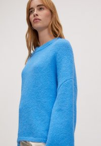 Zacht, helderblauw trui met een ronde halslijn, verlaagde schouders en een gestructureerde afwerking. Casual pasvorm en lange, brede mouwen.