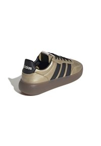 Zapatillas de cuero verde olivo con detalles en negro, parte superior texturizada, tres rayas negras y una suela de goma gruesa y translúcida.