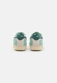 Sneakers in suede verde con una intersuola color crema, caratterizzati da una trama liscia e un design minimalista. Presentano dettagli cuciti e piccole perforazioni.