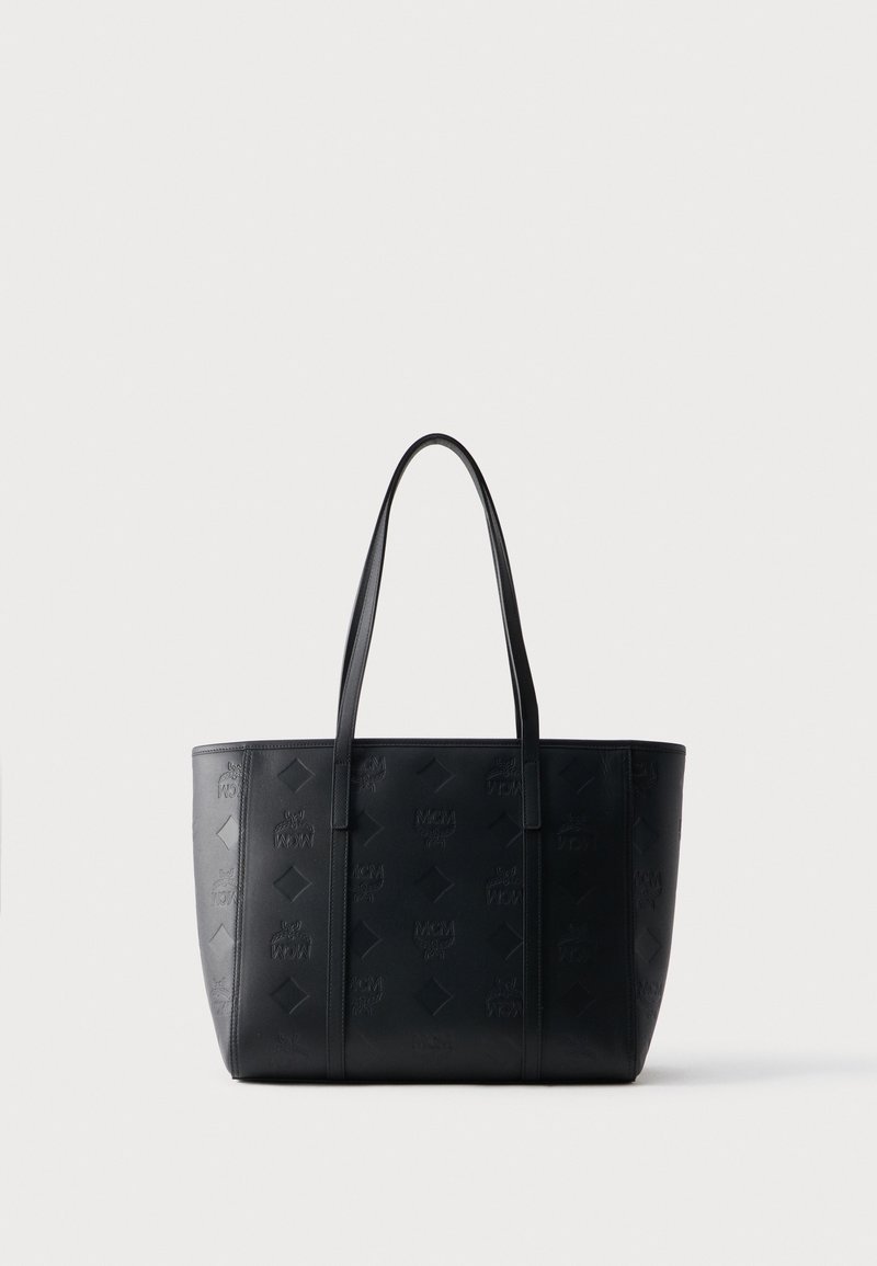 Sac cabas en cuir noir avec logos MCM embossés et motifs en losange, doté de deux longues bandoulières, sur fond blanc uni.