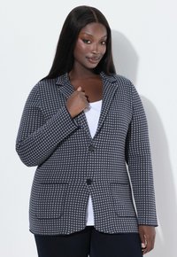 Blazer a quadri grigio e bianco con revers, due bottoni e due tasche frontali. Tessuto texturizzato, vestibilità sartoriale e maniche lunghe.