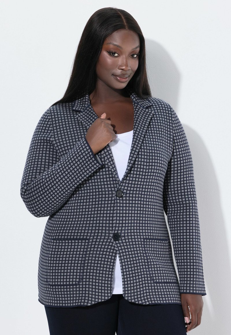 Blazer a quadri grigio e bianco con revers, due bottoni e due tasche frontali. Tessuto texturizzato, vestibilità sartoriale e maniche lunghe.